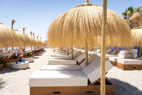 福恩吉罗拉Higuerón Hotel Curio Collection by Hilton的海滩上一排带稻草遮阳伞的沙滩椅