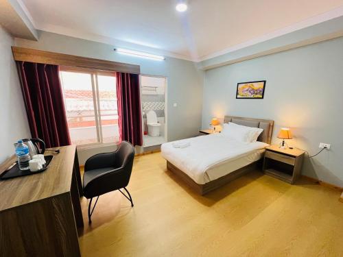 加德满都Boudha Apart Hotel的一间卧室配有一张床、一张书桌和一个窗户。