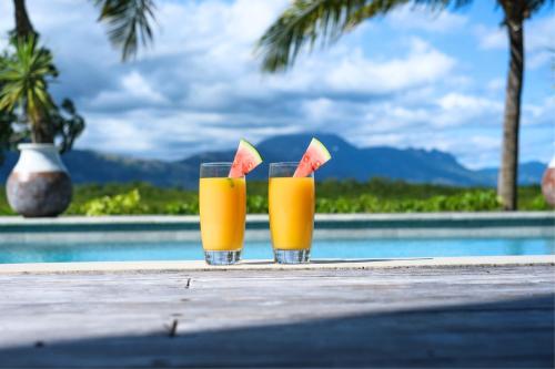 南迪Naisoso Island Villas - Fiji的两杯橙汁和西瓜放在桌旁的游泳池畔