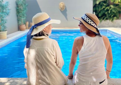 赫雷斯-德拉弗龙特拉Casa Palacio Ánima的两个戴帽子的女人坐在游泳池旁边