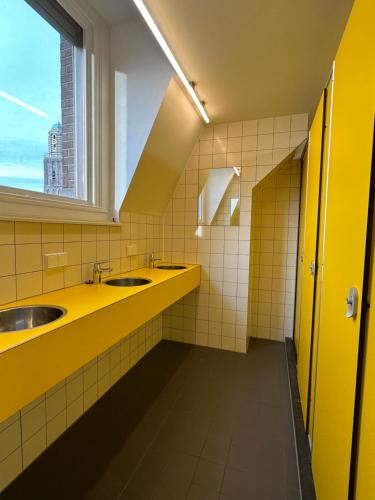 兹沃勒Hostel & Bar De Basis的黄色的浴室设有两个盥洗盆和窗户
