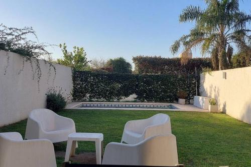 科尔多瓦Casa Pascal, Bº Villa Belgrano的一个带白色椅子和游泳池的花园