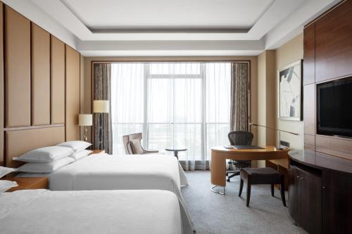胶州青岛胶州绿城喜来登酒店的酒店客房设有两张床、一张桌子和一台电视。