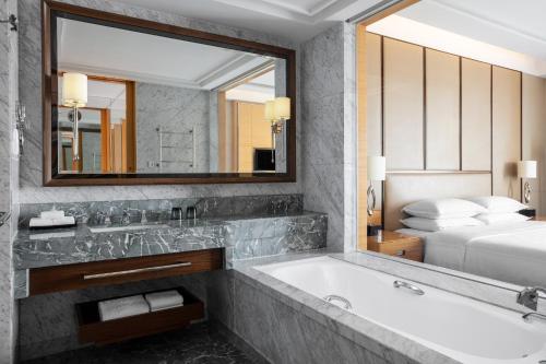胶州青岛胶州绿城喜来登酒店的带浴缸和镜子的浴室以及一张床