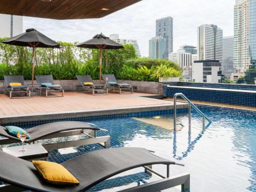 曼谷Pullman Bangkok Hotel G的一座大楼内的游泳池,配有椅子和遮阳伞