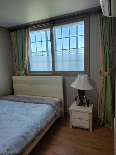 巨济Capri Hakdong Pension的一间卧室设有床、两扇窗户和一盏灯。