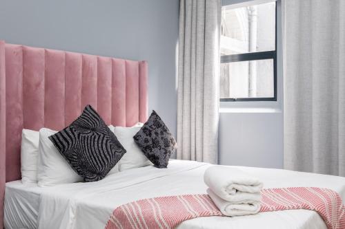 开普敦Cape palm royal guest house的一间卧室配有一张带粉红色床头板和枕头的床。