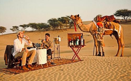 斋沙默尔Sam dunes desert safari camp的一群人坐在沙漠里,带着骆驼