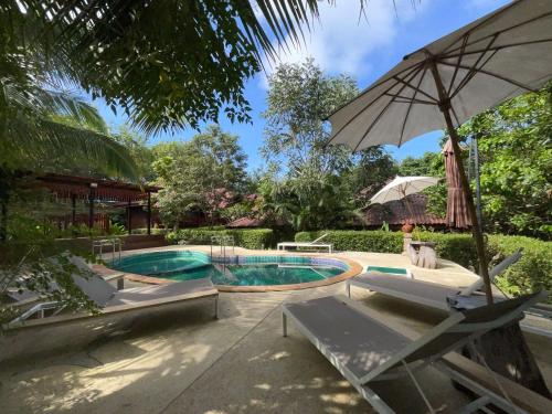 高兰Siam Lanta Resort - SHA Extra Plus的游泳池配有椅子和遮阳伞,旁边还有人坐在椅子上