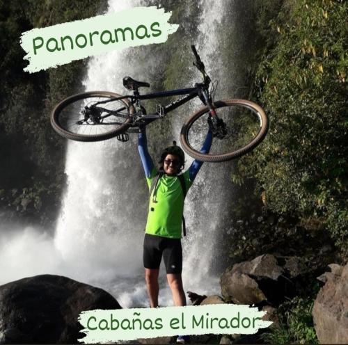 RecintoCabañas el Mirador的把自行车停在瀑布上的人