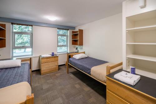 温哥华瓦尼埃学生宿舍帕西斯比特旅馆的一间卧室配有两张床、一张桌子和书架
