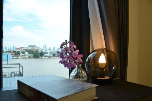 曼谷NORN Riverside Bangkok Hotel - นอนริมน้ำ的书和一束花在桌子上的花瓶,有窗