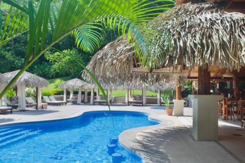 曼努埃尔安东尼奥Hotel Playa Espadilla & Gardens的一个带草伞和椅子的度假游泳池