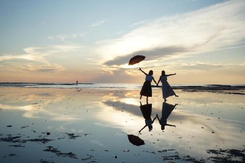 田边市KAMENOI HOTEL Kii-Tanabe的两名妇女在海滩上用遮阳伞散步