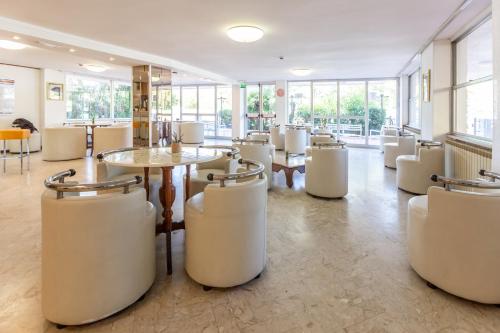 里米尼Hotel Naica的餐厅设有白色的椅子和桌子以及窗户。