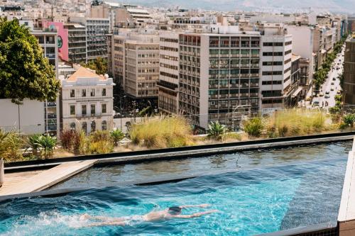 雅典Skylark, Aluma Hotels & Resorts的在建筑物顶部的游泳池游泳的人
