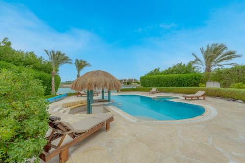 赫尔格达Stunning Villa for Rent in El Gouna HEATED PRIVATE POOL的毗邻带稻草遮阳伞和躺椅的游泳池