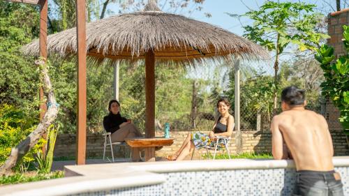 ItauguáLa Casita de Aregua的两个女人坐在泳池旁的太阳伞下