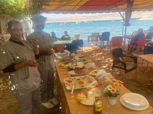 亚喀巴Al-Amer Hostel 2的两个男人站在餐桌前吃着食物