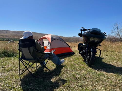 NachesInfidel Acres Motorcycle tent spaces.的坐在帐篷和摩托车旁边的椅子上的人