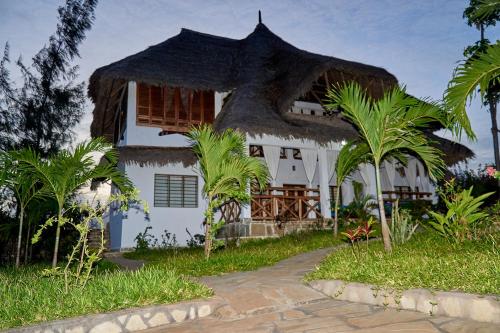 马林迪Beach Way Villa的白色的房子,拥有茅草屋顶和棕榈树