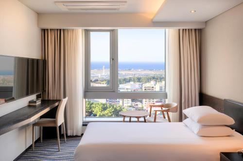 济州市Gloucester Hotel Jeju的酒店客房设有一张床、一张书桌和一个大窗户。