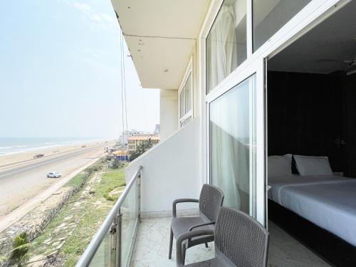 普里Hotel TBS ! PURI all-rooms-sea-view fully-air-conditioned-hotel with-lift-and-parking-facility breakfast-included的一个带一张床和椅子的阳台以及海滩