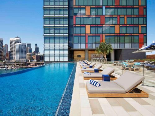 悉尼悉尼达令港索菲特酒店的酒店游泳池设有躺椅,酒店大楼