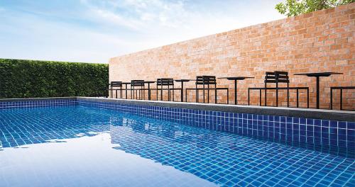 曼那Theorie Hotel Sukhumvit by Tolani - SHA Extra Plus的一个带桌椅的游泳池以及砖墙