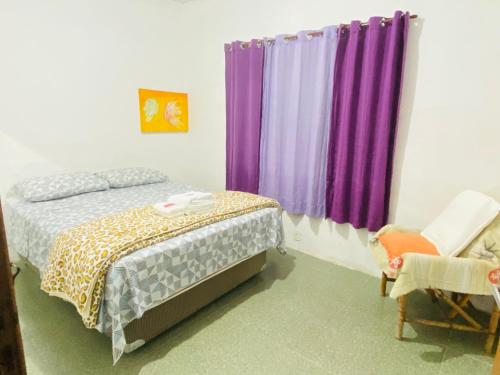 大普拉亚Seu Cantinho na Vila Tupi 3 Dormitórios的一间卧室配有紫色窗帘、一张床和一把椅子