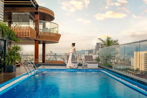 岘港Mercy Emerald Hotel的站在一座建筑物顶部游泳池旁的女人