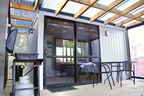 NgaruawahiaThe Bird House Tiny Home的一个带玻璃门和桌椅的屏蔽门廊