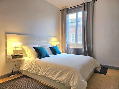 图卢兹L'Idrac, Appartements en Hyper centre的一间卧室配有一张带蓝色枕头的床和一扇窗户。
