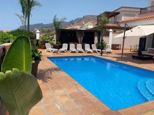 圣地亚哥港Self Catering Luxury Villa in the beautiful area of Puerto Santiago Tenerife with 5 bedrooms 2 Sofabeds for up to 10 guests private swimming pool and many other activities to entertain the family Secure parking for 2 cars and disabled access throughout的一个带椅子的游泳池以及一座房子