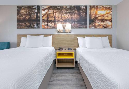 格林维尔Days Inn by Wyndham Greenville MS的酒店客房带两张床,中间还有一张黄色的桌子。