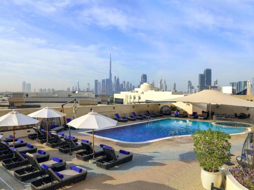 迪拜Mövenpick Hotel & Apartments Bur Dubai的一座大楼内的游泳池,配有椅子和遮阳伞