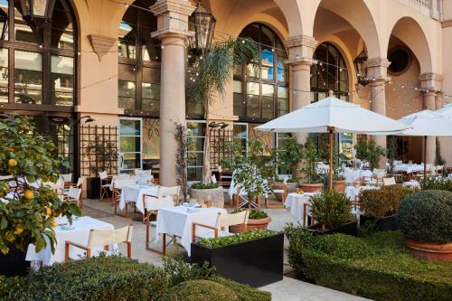 洛杉矶The Maybourne Beverly Hills的大楼前的餐厅,配有桌子和遮阳伞