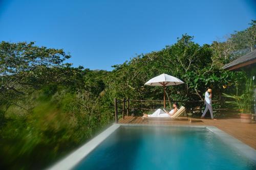BumbangTUNAK Resort Lombok的两人坐在游泳池旁的伞下