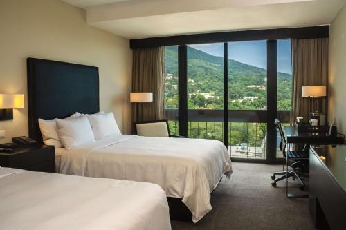 圣萨尔瓦多Hilton San Salvador的酒店客房设有两张床和大窗户。