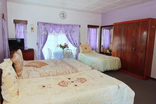 努沃勒埃利耶Heavenly Home Inn的一间卧室设有两张床和一个带紫色窗帘的窗户。