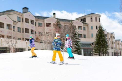 北塩原村EN RESORT Grandeco Hotel的三个孩子在雪中滑雪,在建筑物前