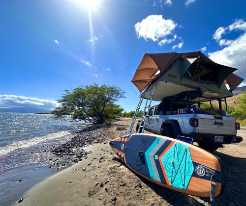 帕依亚Embark on a journey through Maui with Aloha Glamp's jeep and rooftop tent allows you to discover diverse campgrounds, unveiling the island's beauty from unique perspectives each day的停在海滩上的卡车,上面有船