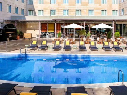 科尔内拉德罗布雷加特诺富特巴塞罗那科内拉酒店的一座带桌椅的游泳池以及一座建筑