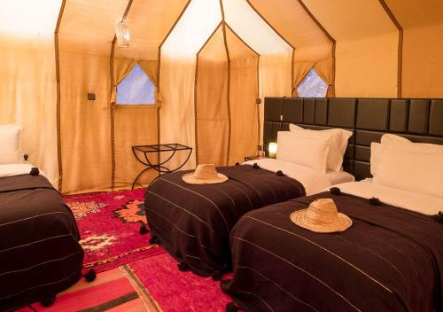 扎古拉Sahara Relax Camps的帐篷内的两张床,配有帽子