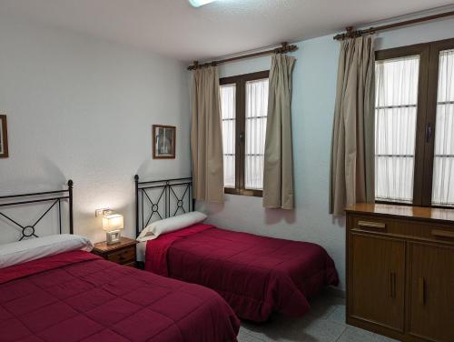 格拉纳达纳瓦罗拉莫斯城市旅馆的一间卧室设有两张带红色床单和窗户的床。