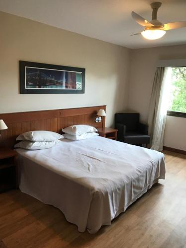格拉玛多Flat em Gramado的卧室配有一张白色大床和一把椅子