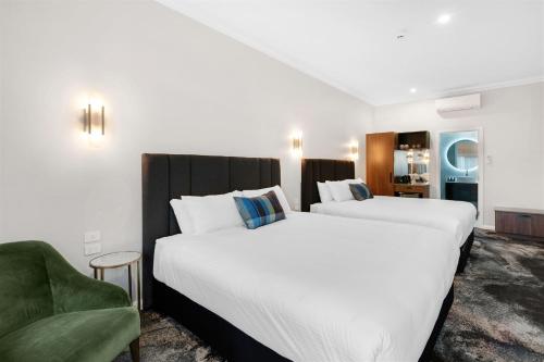 沃加沃加St Hugh Hotel Wagga Wagga的两张位于酒店客房的床,配有绿色椅子