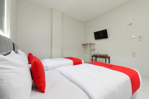 HajimanaRedDoorz near GSG UNILA Lampung的客房内的两张白色床和红色枕头