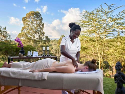 纳纽基费尔蒙特山肯尼亚野生动物园俱乐部酒店的一位女士躺在按摩床上,有一位治疗师