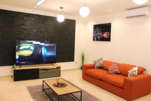 科托努RESIDENCE MH SERVICES Cotonou的客厅配有橙色沙发和平面电视。